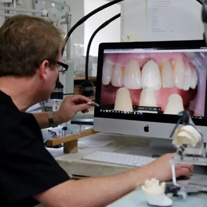 In our lab: a technician compares a shade tab with photographs of a patient's teeth on screen